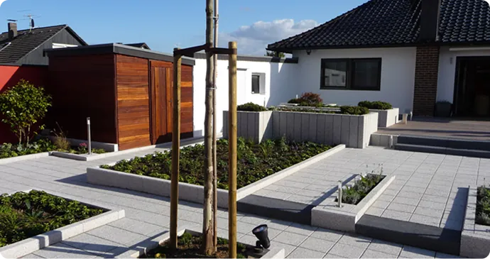 Terrasse mit Pflasterflächen, Hochbeeten und neu gepflanzten Bäumen