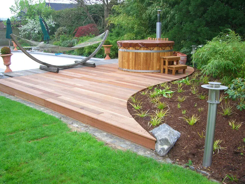 Holzterrasse mit Hängematte und Badefass in einem bepflanzten Garten